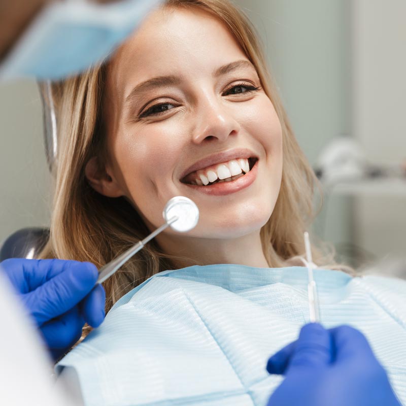 Image of satisfied young woman sitting in dental chair at medical center while professional doctor fixing her teeth