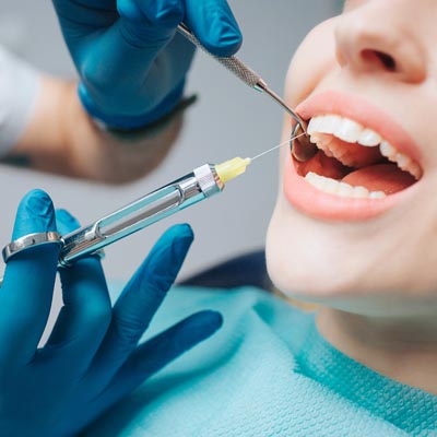 Close up of dentist's hands holding tool and syringe in hands. Pain killer in action. Female client keep mouth opened. Beautiful smile and white teeth. Cut view