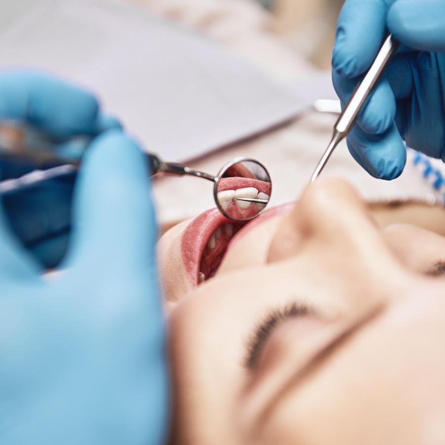Close-up of woman opening her mouth wide during inspection of oral cavity. Dentist is checking up her teeth using dental tools. Medicine and health care concept. Focus on dental tools. Horizontal shot